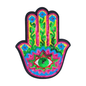 May include: A decorative Hamsa hand patch with a black outline. The design incorporates a central eye symbol, surrounded by pink, blue, green, and yellow patterns. The hand's fingers are decorated with floral and dot details, creating a vibrant accessory.