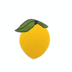 May include: Embroidered patch of a yellow lemon with a green leaf. The lemon is a bright yellow colour with a textured surface. The leaf is green with black outlining. The patch is likely for clothing or accessories.