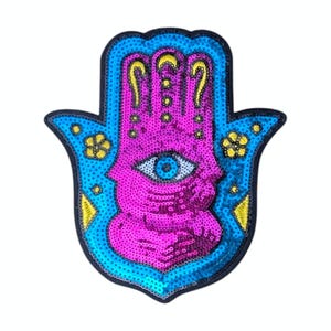 May include: A sequined Hamsa hand patch in shades of blue, pink, and yellow. The hand features an eye in the centre and decorative floral accents. The patch is outlined in black.