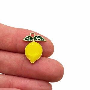 Puede incluir: Un peque&ntilde;o dije con forma de lim&oacute;n que presenta un cuerpo de esmalte amarillo brillante con un borde de metal dorado. En la parte superior, tiene dos hojas de esmalte verde oscuro y un peque&ntilde;o aro de metal dorado para colgar.