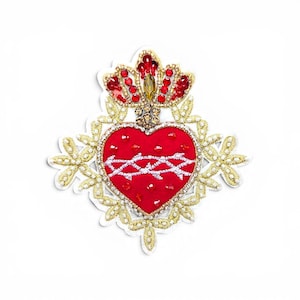 May include: A decorative patch featuring a red fabric heart adorned with red beads and a white embroidered crown of thorns. The heart is surrounded by gold metallic embroidery, clear crystals, and a top crown element with red and amber-coloured stones.