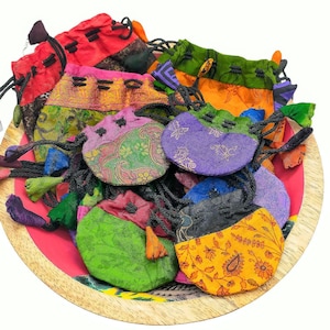 May include: A selection of small, colourful drawstring pouches in shades of red, pink, green, purple, and yellow. The pouches, made from patterned fabric, are arranged on a wooden tray with a pink and red base.