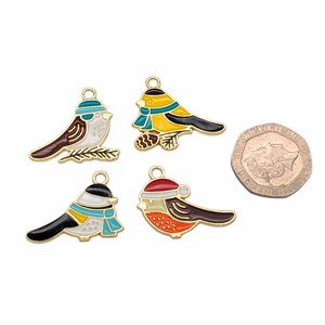 May include: Four gold-tone metal charms shaped like birds wearing winter accessories. The birds are painted in various colors, including red, yellow, blue, white, and black. The charms are approximately the size of a British one pound coin.