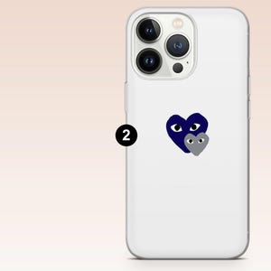 Może przedstawiać: Białe etui na telefon z granatowym wzorem serca i mniejszym szarym sercem. Etui ma przezroczysty, ochronny design i jest wykonane z wytrzymałego materiału. Etui posiada wycięcie na aparat i osłony przycisk&oacute;w.