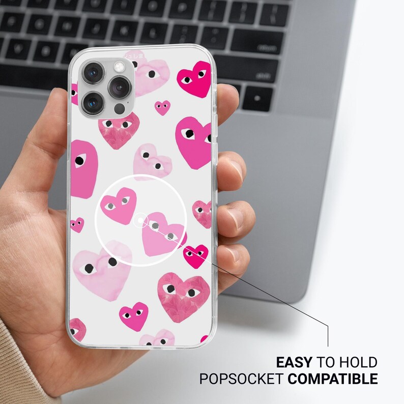 Może przedstawiać: Przezroczyste etui na telefon z wzorem r&oacute;żowych serc z oczami na białym tle. Etui posiada popsocket i tekst "EASY TO HOLD POPSOCKET COMPATIBLE".