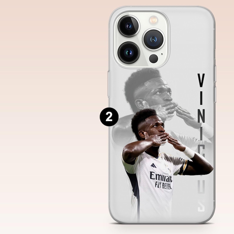 May include: A clear smartphone case featuring a graphic of a soccer player in a white jersey kissing their fingers. The player is shown in both a full-color foreground and a faded black and white background. The text VINICIUS is printed vertically.
