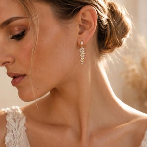 May include: A gold-toned drop earring featuring a marquise-cut stone at the top, connected to a delicate, leaf-shaped dangle composed of multiple small, clear, marquise-cut stones arranged in a cascading, branch-like pattern.