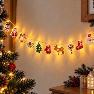 Puede incluir: Una guirnalda de luces LED navideñas con figuras de madera recortadas de un muñeco de nieve, Santa Claus, una campana, una vela, un árbol, un guante, un reno, un bastón de caramelo y un calcetín, iluminadas por una luz blanca cálida.