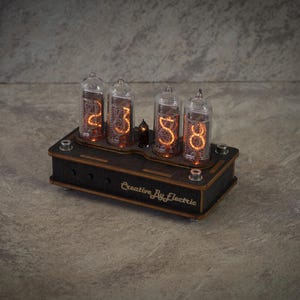 May include: A vintage digital clock featuring four glass tubes showing the time "23:58" in orange digits. The clock sits on a dark wooden base, with the text "Creative By Electric" visible.