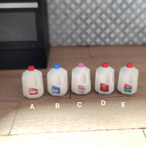May include: Miniature white plastic milk jugs with colorful labels and red, blue, and pink caps. The jugs are labeled A, B, C, D, and E. The jugs are on a wooden surface.