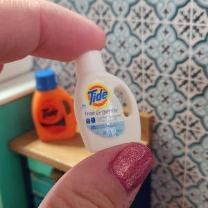 May include: A miniature white plastic bottle of Tide laundry detergent with a blue label that says "free & gentle".