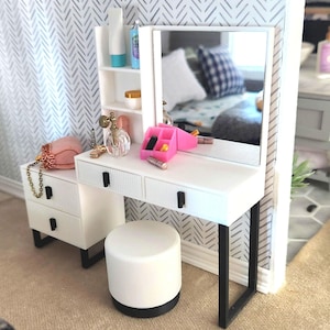 May include: White vanity set with a mirror, three drawers, and a stool. The vanity has black metal legs and a white countertop. There are pink makeup organizers on the countertop.