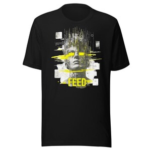 Könnte beinhalten: Ein schwarzes Kurzarm-T-Shirt mit einem Grafikdruck eines menschlichen Gesichts mit digitalem Glitch-Effekt. Das Design zeigt leuchtend gelbe horizontale Streifen über den Augen und das Wort FEED in gelber Schrift unten mittig.