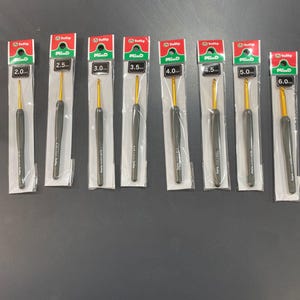 May include: A collection of Tulip Mind crochet hooks in various sizes, ranging from 2.0 mm to 6.0 mm. Each hook has a gold-colored hook and a dark gray handle, packaged in individual clear plastic sleeves with red and green labels.