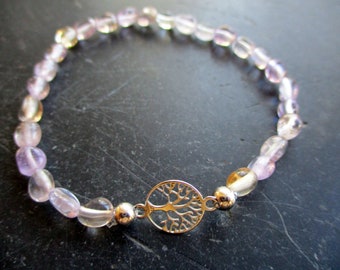 May include: A beaded bracelet featuring translucent, light purple and pale yellow tumbled gemstone beads arranged in a circular pattern. The bracelet includes a central circular silver-toned metal charm depicting a detailed tree silhouette.