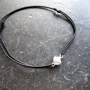 Può includere: Braccialetto con cordino nero con un piccolo ciondolo a forma di conchiglia color argento. Il braccialetto è regolabile con una chiusura a nodo scorrevole. Il ciondolo a forma di conchiglia è dettagliato e aggiunge un tocco nautico.