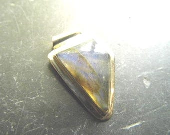 May include: A triangular pendant featuring a polished labradorite stone with iridescent blue and gold flashes, encased in a smooth, polished metal setting with a top bail for hanging. The stone displays natural color variations and a reflective surface.
