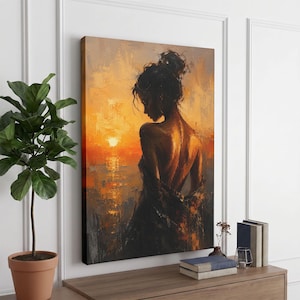 Op de afbeelding: Een rechthoekige canvas print met een impressionistisch olieverfschilderij van een persoon van achteren gezien, staand tegen een levendige oranje en gele zonsondergang boven water. Het figuur heeft donker haar in een knot en draagt een donker kledingstuk.