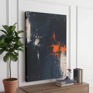 May include: A rectangular canvas wall art piece featuring a dark navy blue background with abstract vertical streaks of white and a prominent splash of bright orange paint. The composition displays a textured, layered appearance with visible brushstrokes.