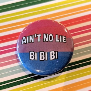 May include: A round button with a pink, purple, and blue design. The button has the text "Ain't no lie" in white letters on the pink and purple section and "Bi Bi Bi" in white letters on the blue section.