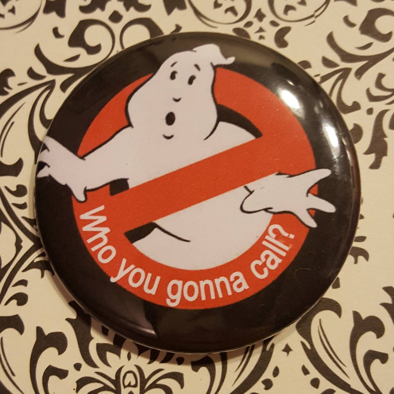 K&ouml;nnte beinhalten: Ein schwarzer und roter Knopf mit einer wei&szlig;en Geisterfigur und dem Text "Who you gonna call?" Der Geist befindet sich in einem roten Kreis mit einem diagonalen roten Strich.