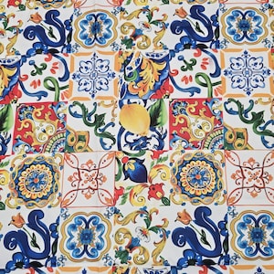 Può includere: Un tessuto colorato a fantasia con un design patchwork di piastrelle quadrate. Ogni piastrella mostra intricati motivi floreali e geometrici nei toni del blu, giallo, arancione e rosso su sfondo bianco. È visibile anche un limone con foglie verdi.