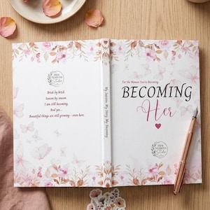 May include: A hardcover book titled Becoming Her with a white cover featuring pink floral illustrations and butterflies. The back cover text reads: Brick by brick. Season by season. I am still becoming. And yes... Beautiful things are still growing.