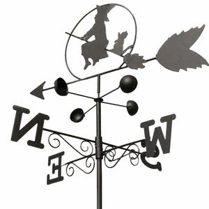 May include: A black metal weather vane featuring a silhouette of a figure on a broomstick with a cat inside a circular frame. The structure includes directional letters N, E, S, W, a central vertical pole, and a rotating anemometer with four cups.
