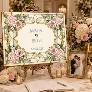 K&ouml;nnte beinhalten: Ein rechteckiges Schild mit einem Buntglasmuster, das in den Ecken rosa Rosen und Hortensienbl&uuml;ten zeigt. In der Mitte befindet sich ein wei&szlig;es Feld mit dem Text JAMES & ELLA und dem Datum 6.10.2027. Das Schild steht auf einer verzierten goldenen Staffelei.