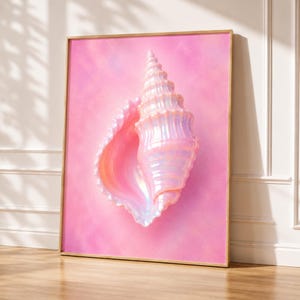 May include: A framed wall art print featuring a large, iridescent seashell with a pearlescent finish in shades of pink, peach, and white. The shell is centered against a soft, solid pink background, encased in a thin, metallic gold frame.