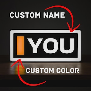 May include: A rectangular LED sign featuring a black background with a white border. The text "I YOU" is displayed in white, with the letter "I" replaced by a vertical orange rectangle. Red arrows point to the text and the orange color.