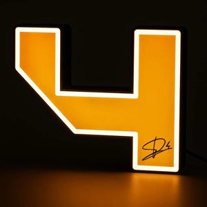 May include: A glowing, illuminated sign in the shape of the number four. The sign features a bright orange center panel surrounded by a white border, with a black signature located in the lower right corner of the number's structure.