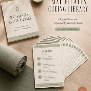 May include: A Mat Pilates Cueing Library set featuring a printed manual and a deck of instructional cards. The cards display text including 'HUNDRED', 'TEACHING INTENT', 'KEY CUE', 'MODIFICATIONS', and 'PROGRESSION'. A rolled sage green yoga mat is visible.