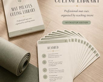 May include: A Mat Pilates Cueing Library set featuring a printed manual and a deck of instructional cards. The cards display text including 'HUNDRED', 'TEACHING INTENT', 'KEY CUE', 'MODIFICATIONS', and 'PROGRESSION'. A rolled sage green yoga mat is visible.