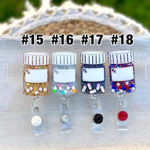 May include: Four prescription bottle-shaped badge reels with glitter and decorative accents. Each reel has a different color scheme, including gold, silver, navy, and red. The reels are labeled with the numbers #15, #16, #17, and #18.