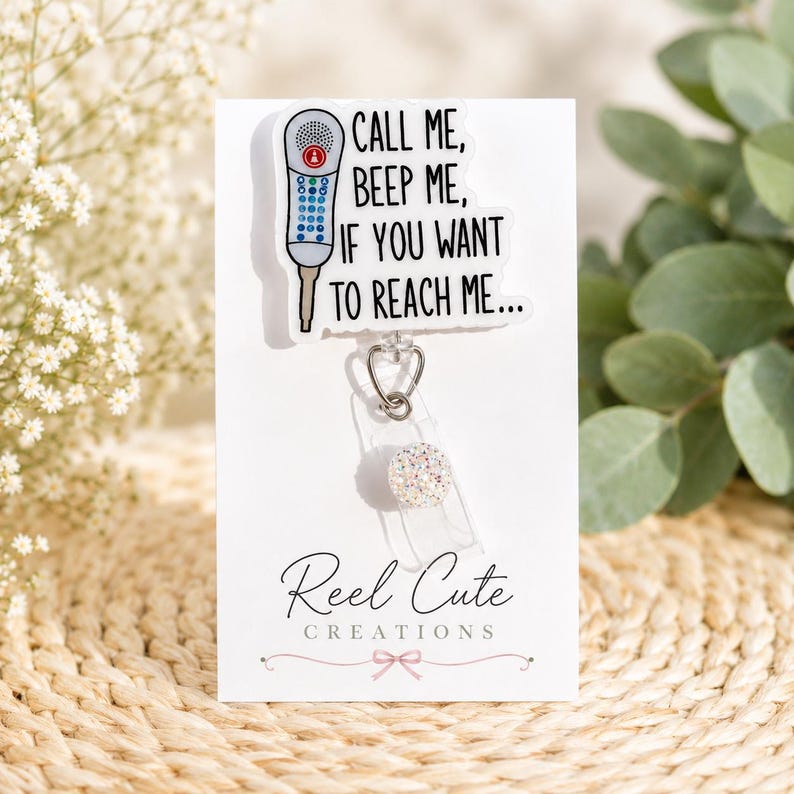 May include: A white badge reel with the text "CALL ME, BEEP ME, IF YOU WANT TO REACH ME...". The badge features a cartoon phone graphic and a glittery, round accent. The Reel Cute Creations logo is at the bottom.
