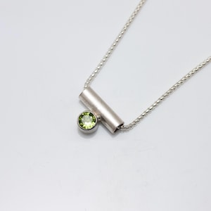 May include: A silver necklace with a small green gemstone and a silver bar pendant.
