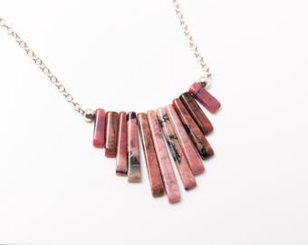 May include: A silver chain necklace featuring a pendant of graduated, rectangular pink and brown stones. The stones are arranged in a fan shape, with a small silver bead at the top of the pendant. The necklace is displayed on a white background.