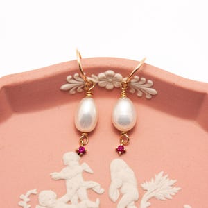 May include: A pair of gold earrings with a white pearl drop and a small pink gemstone accent.