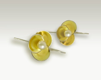May include: A pair of gold and silver earrings with a pearl in the center of each flower-shaped design.