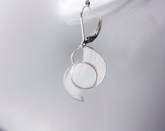 May include: Silver earrings with a geometric design featuring a circle and a crescent shape.