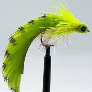 May include: A vibrant, handmade fishing fly with a bright chartreuse body speckled with black markings. The fly features a yellow head and iridescent accents, mounted on a black hook. This fly is designed for attracting fish.