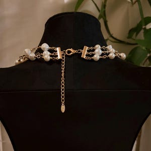 Puede incluir: Un collar de m&uacute;ltiples hileras con perlas blancas artificiales intercaladas con cadenas de metal dorado. La pieza incluye un cierre de mosquet&oacute;n dorado, una cadena extensora corta y una peque&ntilde;a etiqueta met&aacute;lica ovalada al final.