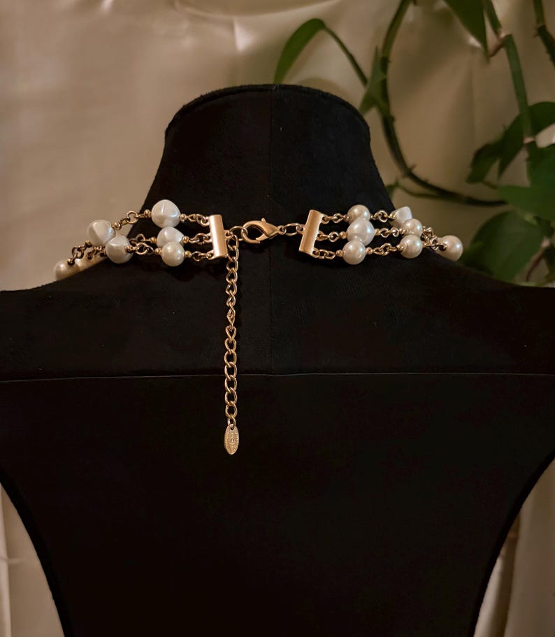 Puede incluir: Un collar de m&uacute;ltiples hileras con perlas blancas artificiales intercaladas con cadenas de metal dorado. La pieza incluye un cierre de mosquet&oacute;n dorado, una cadena extensora corta y una peque&ntilde;a etiqueta met&aacute;lica ovalada al final.