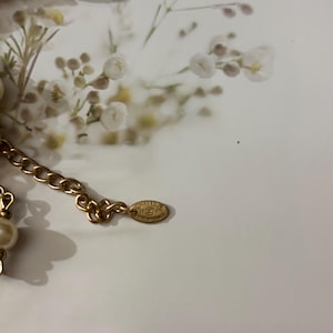Puede incluir: Un collar de cadena en tono dorado con perlas de imitaci&oacute;n color crema y detalles circulares en negro y dorado. El collar incluye una peque&ntilde;a etiqueta met&aacute;lica ovalada grabada con el logo de Chanel y el texto Made in France en los eslabones.