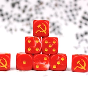 May include: A collection of red six-sided dice arranged in a pyramid formation. Two dice feature a yellow hammer and sickle symbol on one face, while the others display yellow pips representing the numbers one, two, three, four, and five.