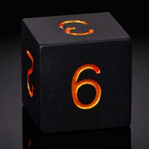 以下が含まれることがあります： マットブラックの6面ダイスで、各面に数字が刻まれています。前面の大きな「6」を含む数字は、内部から温かみのあるオレンジ色の光で照らされており、暗い表面とのコントラストが際立っています。