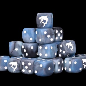 May include: A stack of blue and grey marbled six-sided dice with white pips. Several dice feature a white shark silhouette replacing the number one. The dice have a smooth, polished finish and are arranged in a pyramid shape against a black background.