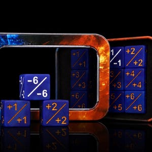 Könnte beinhalten: Ein Set aus blauen sechsseitigen Würfeln mit goldenen und weißen Zahlenmarkierungen, die positive und negative Werte zeigen, welche durch eine diagonale Linie getrennt sind. Die Würfel liegen neben einer rechteckigen Metalldose mit Flammenmuster.