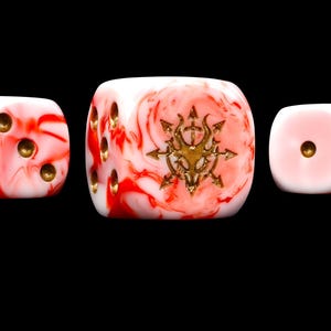 May include: Three six-sided dice featuring a white and red marbled pattern. The dice have gold-colored pips and a central gold-colored symbol on the face of the largest die, depicting a stylized eight-pointed star with a central skull motif.